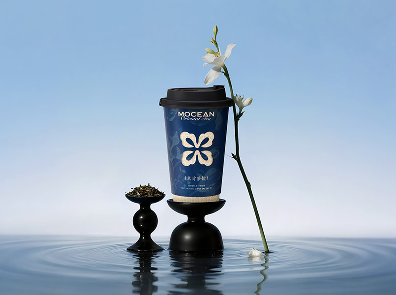 A Mocean cup on a black pedestal over still water, beside a jasmine stem